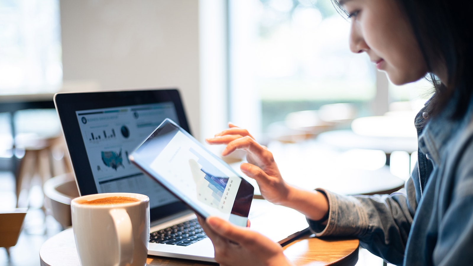 Woman using a digital tablet and laptop in a café and looking at charts